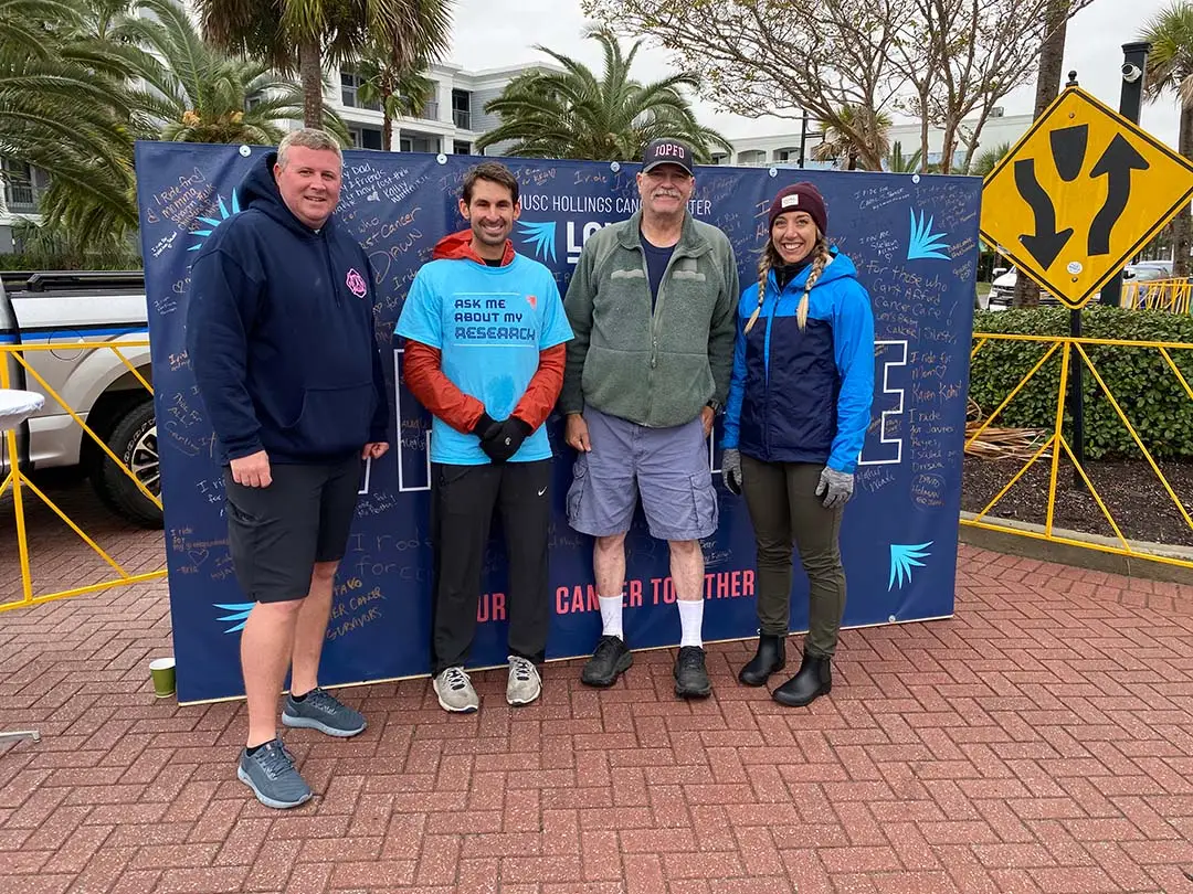 4 people pose in front of Why I Ride wall