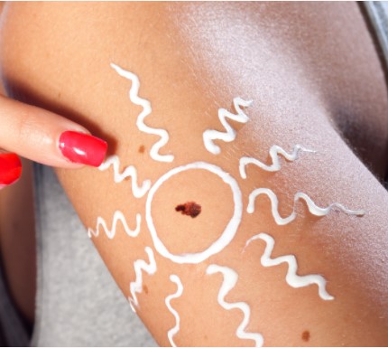 close up of an arm with sunscreen applied in a sun design with a finger pointing at it