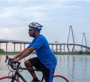 man sits on his bike with the ravenel bridge in the background