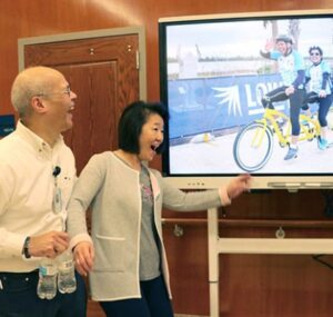 jose and wendy perey smile as they see a photo of themselves on a tv screen