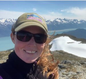 Lucy Boyce hikes in Alaska with water and mountains behind her