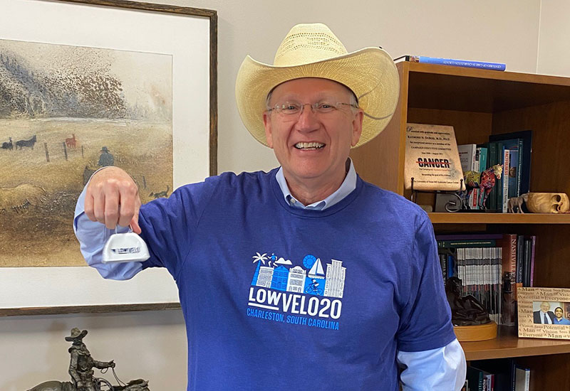 Dr. Raymond DuBois rings a Lowvelo cowbell wearing a cowboy hat and Lowvelo shirt