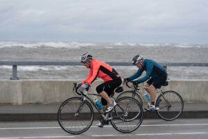 two riders pedal past the ocean