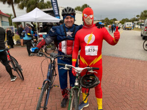 two riders in superhero costumes stand with their bikes