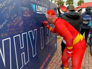 rider dressed in superhero costume writes message on Why I Ride wall