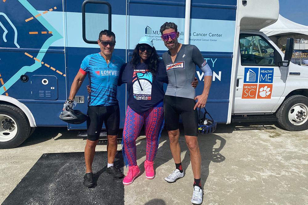 3 cyclists standing in front of a medical van