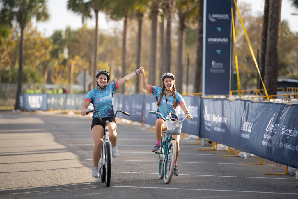 two women crossing finish line on bikes holding hands in air