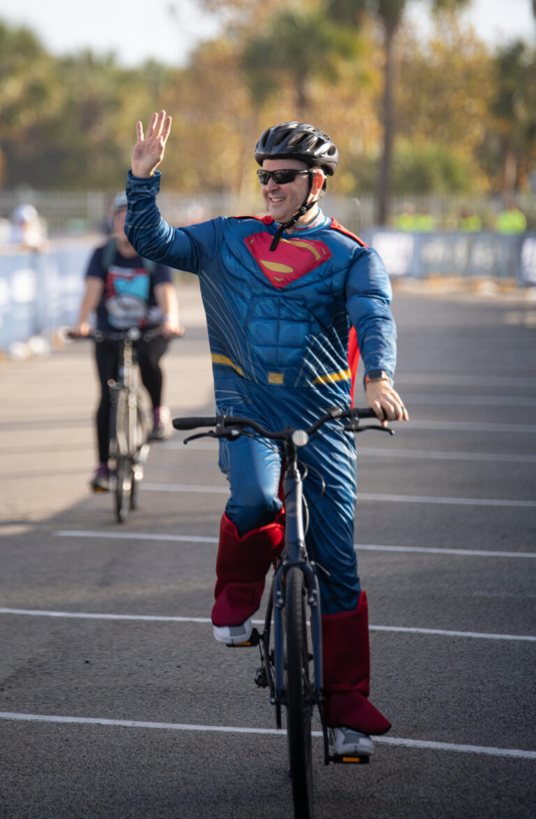 man crossing finish line on bike in superman costume