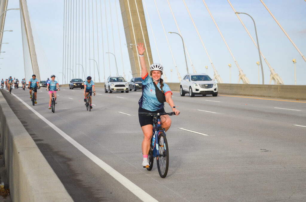 female on bike raising hand as she coasts down Ravenel Bridge