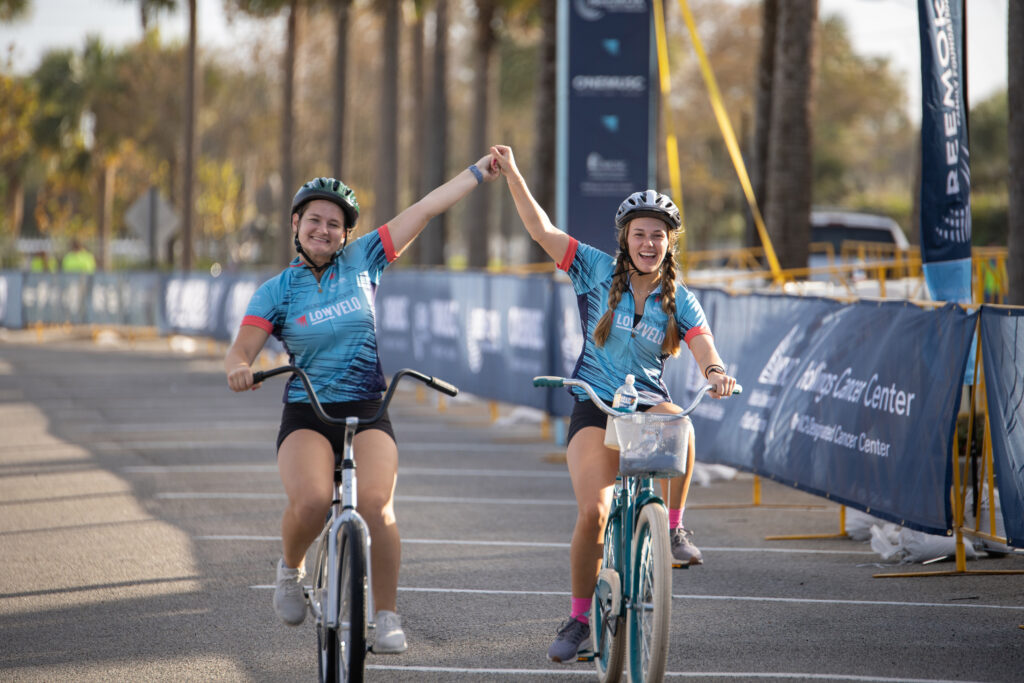 two women holding hands as they cross finish line on bikes