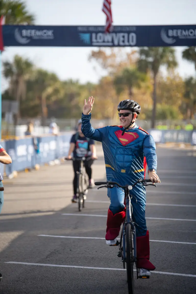 man in superman costume waves as he crosses the Lowvelo finish line