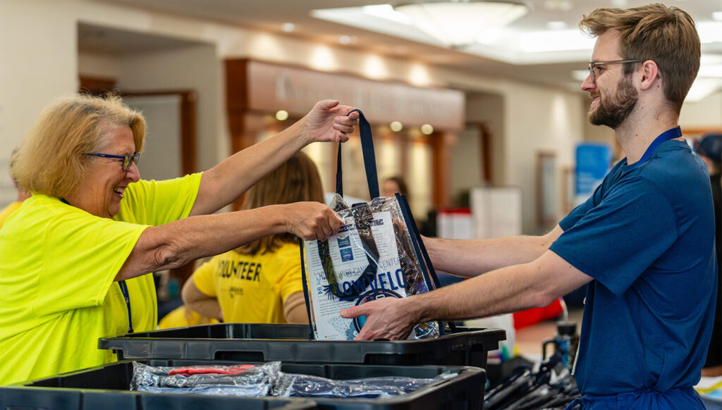 female lowvelo volunteer wearing a yellow shit handing a clear lowvelo swag bag to a male participant