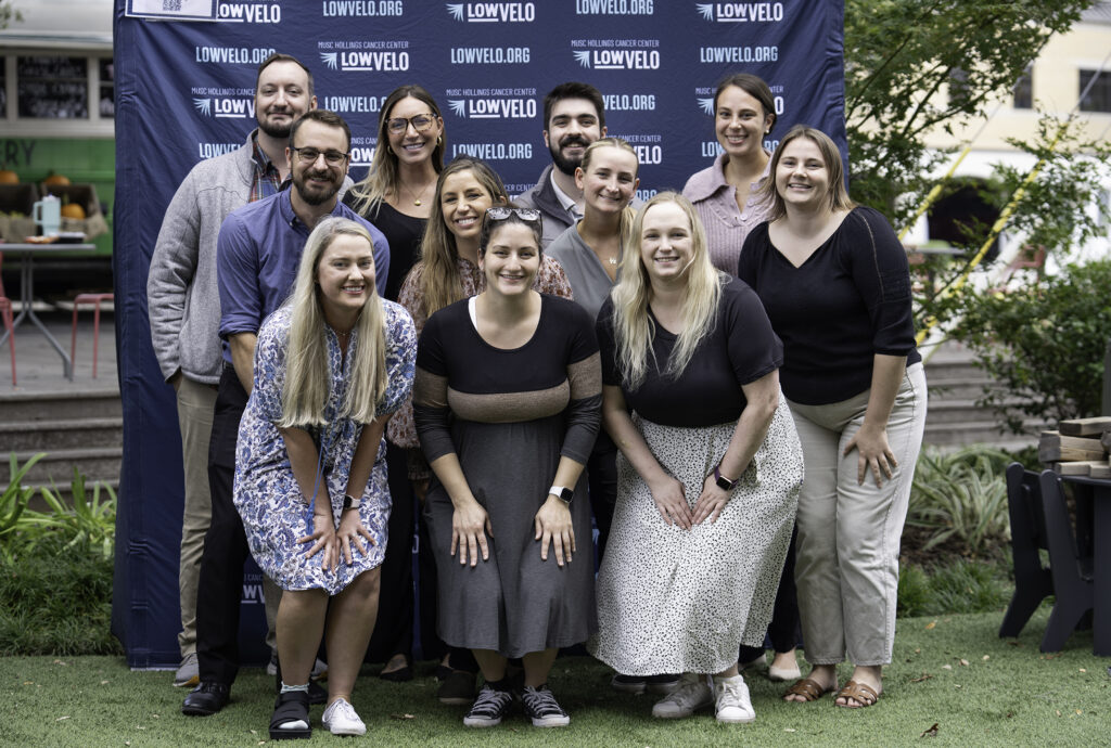 A group of coworkers pose in front of a Lowvelo backdrop during Glow Blue Week on the MUSC Greenway