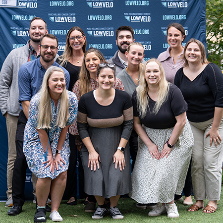 group of coworkers stands in front of Lowvelo wall at Glow Blue Festival on the MUSC Greenway