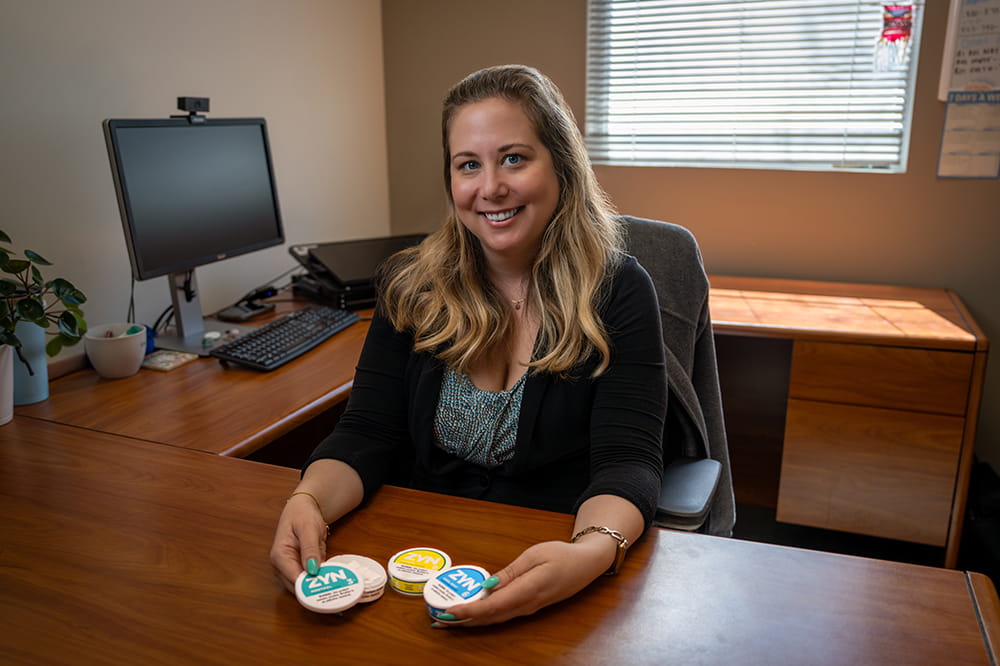 Woman sitting at a desk with oral nicotine pouches on the desk in front of her