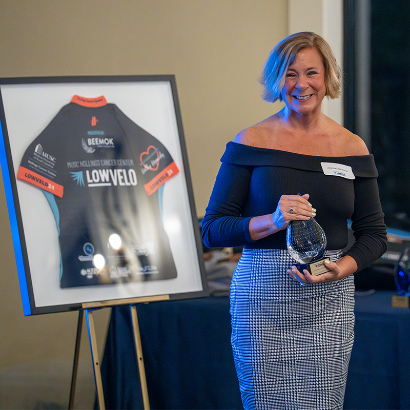 woman stands next to a Lowvelo jersey holding a high tide club award