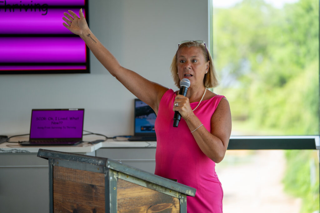 woman in bright pink dress raises her arm as she speaks from a podium