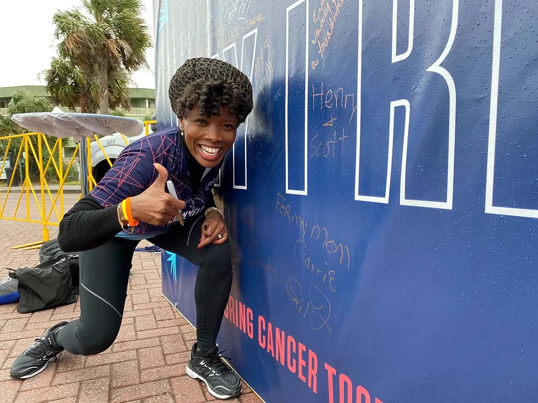 woman stands by Why I Ride wall giving thumbs up