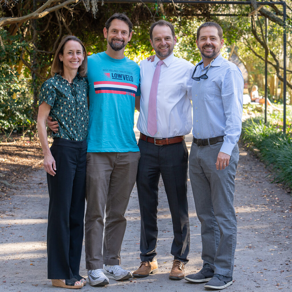 Four people stand together smiling in a park. One is wearing a Lowvelo t shirt.