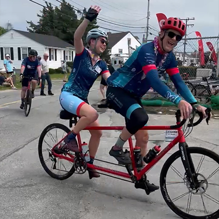Two people ride a tandem bicycle smiling