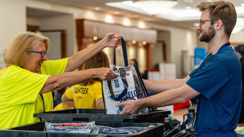 female lowvelo volunteer wearing a yellow shit handing a clear lowvelo swag bag to a male participant