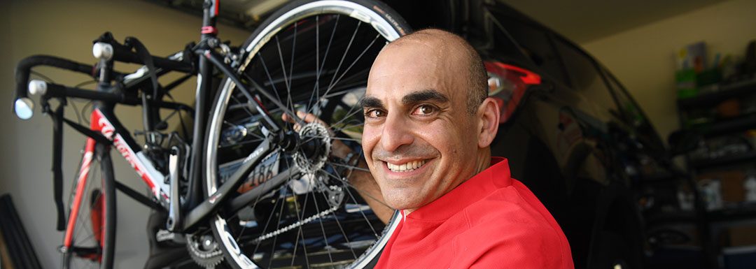 smiling man stands next to his bike on a car rack
