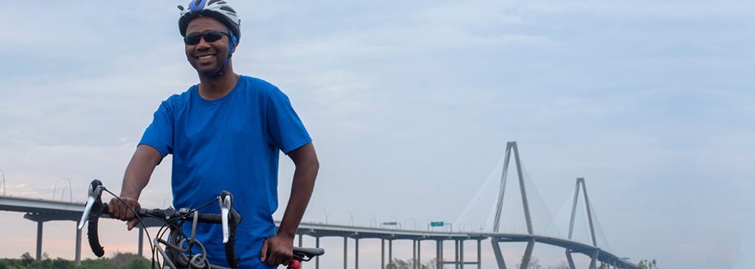 man stands with his bike with the ravenel bridge in the background